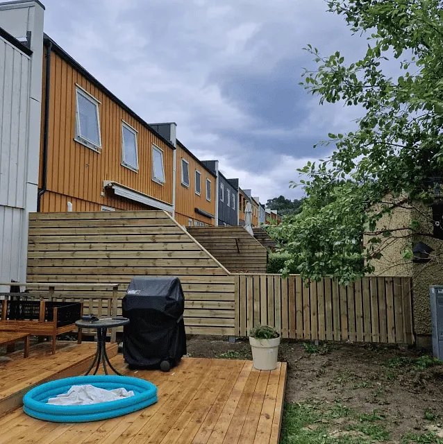 Treterrasse med utemøbler, grill og lite basseng foran rekkehus i tre.